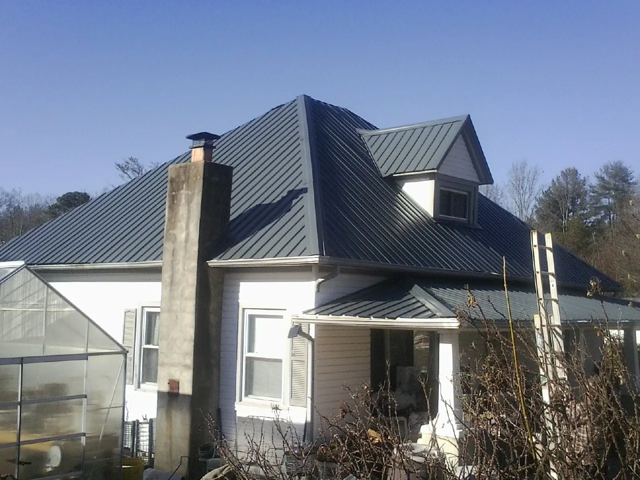 Dark blue standing seam metal roof on a white farmhouse with dormer — Slate & Tile Roof Repair by Roofing Brothers in Nachusa