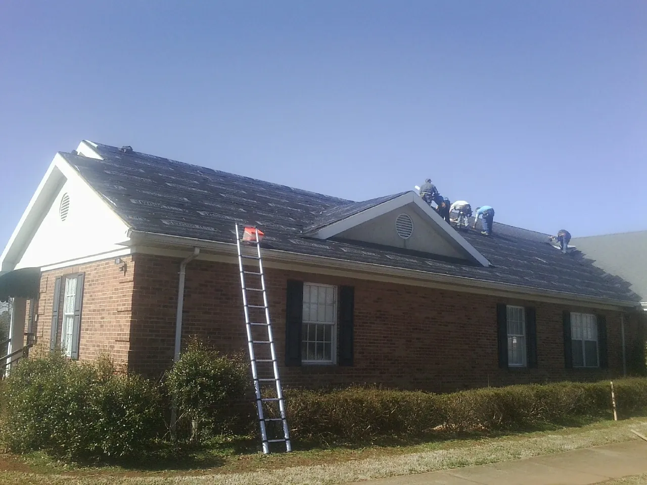 Crew tearing shingles off a brick ranch roof with a ladder set — Metal Roof Repair work by our crew in Nachusa
