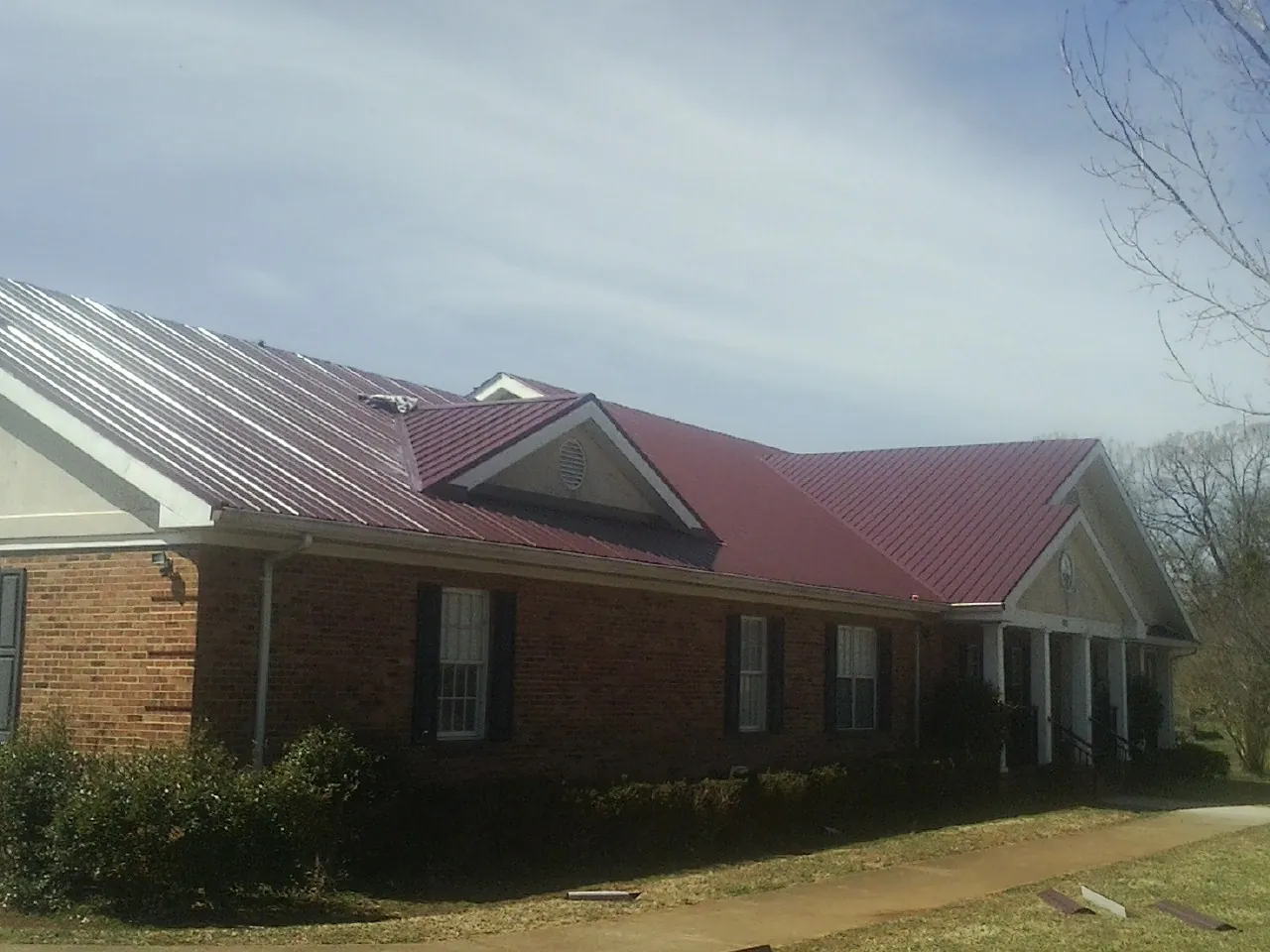 Red metal roof with gabled entries on a long brick building, from a Hail Damage Roof Repair job in Nachusa