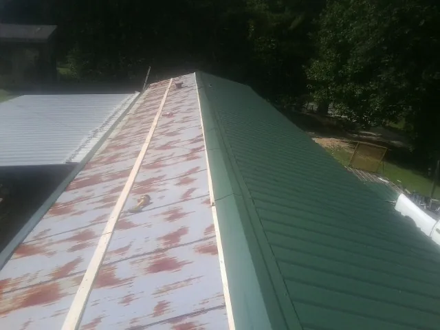 Old rusted panels beside newly installed green metal roofing — Wind Damage Roof Repair by Roofing Brothers in Nachusa