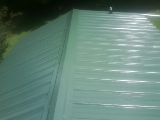 New green metal panels meeting at the ridge of a roof — Flat Roof Repair work by our crew in Nachusa