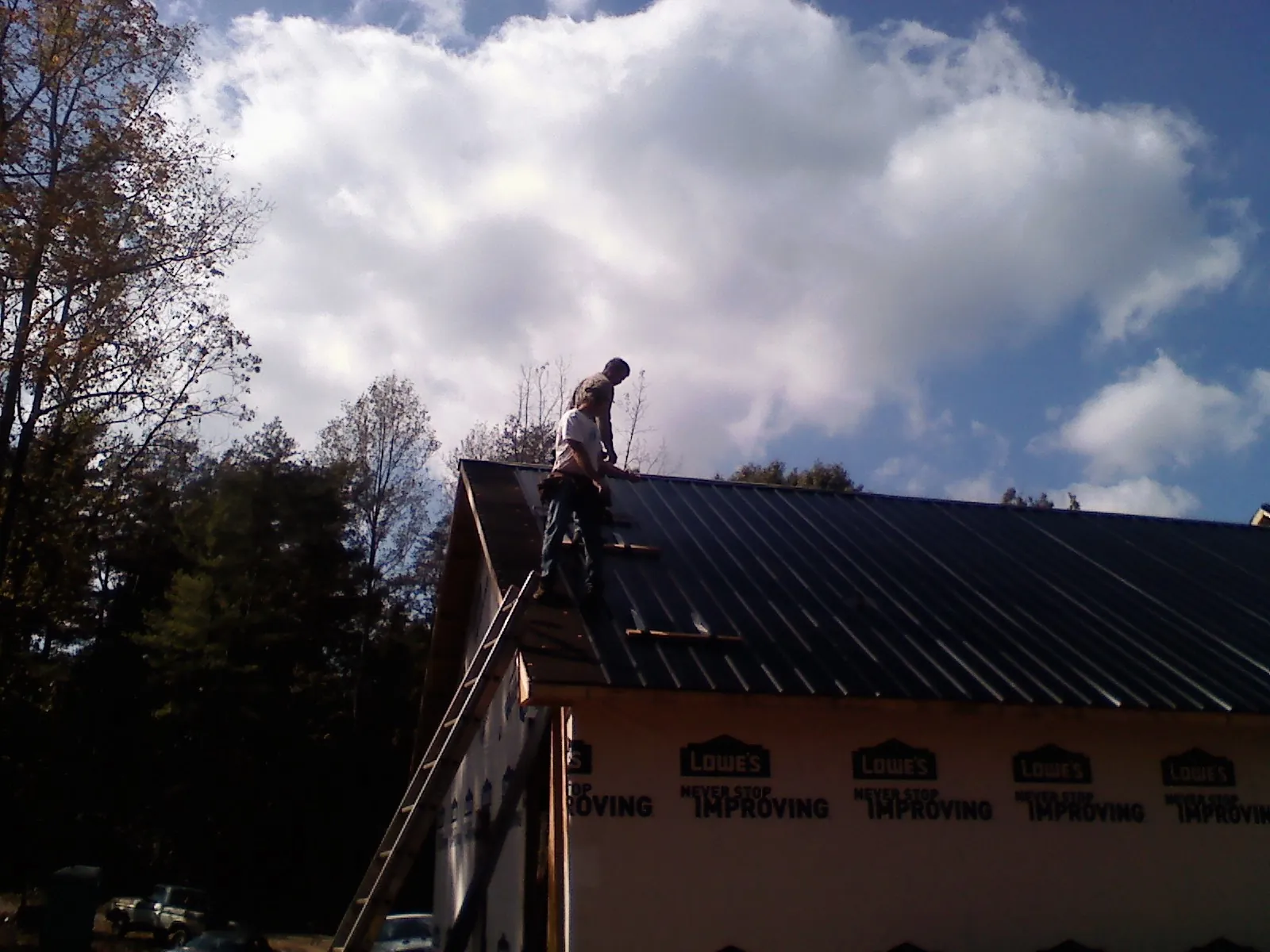 Roofer fastening dark metal panels high against a cloudy sky, from a Roof Inspection job in Nachusa